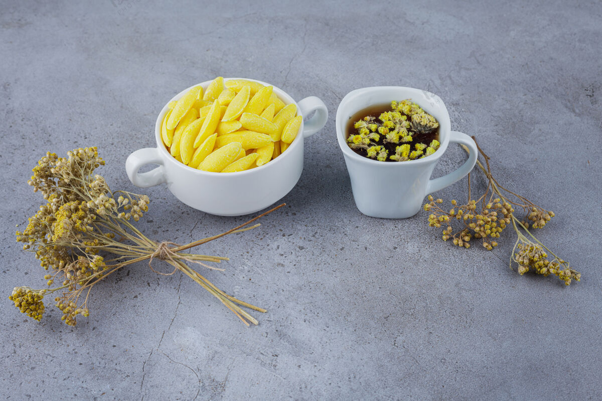 草药一杯热茶和一碗白的黄色糖果放在石头上茶干的糖果