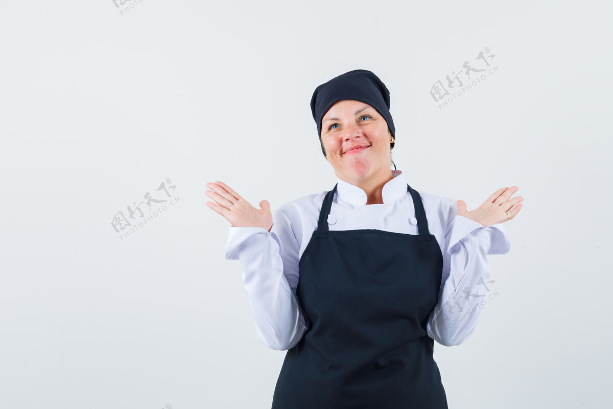 健康金发女子摊开手掌 表现出无助的姿态 身穿黑色厨师制服 看起来很高兴 正面视图魅力化妆女性