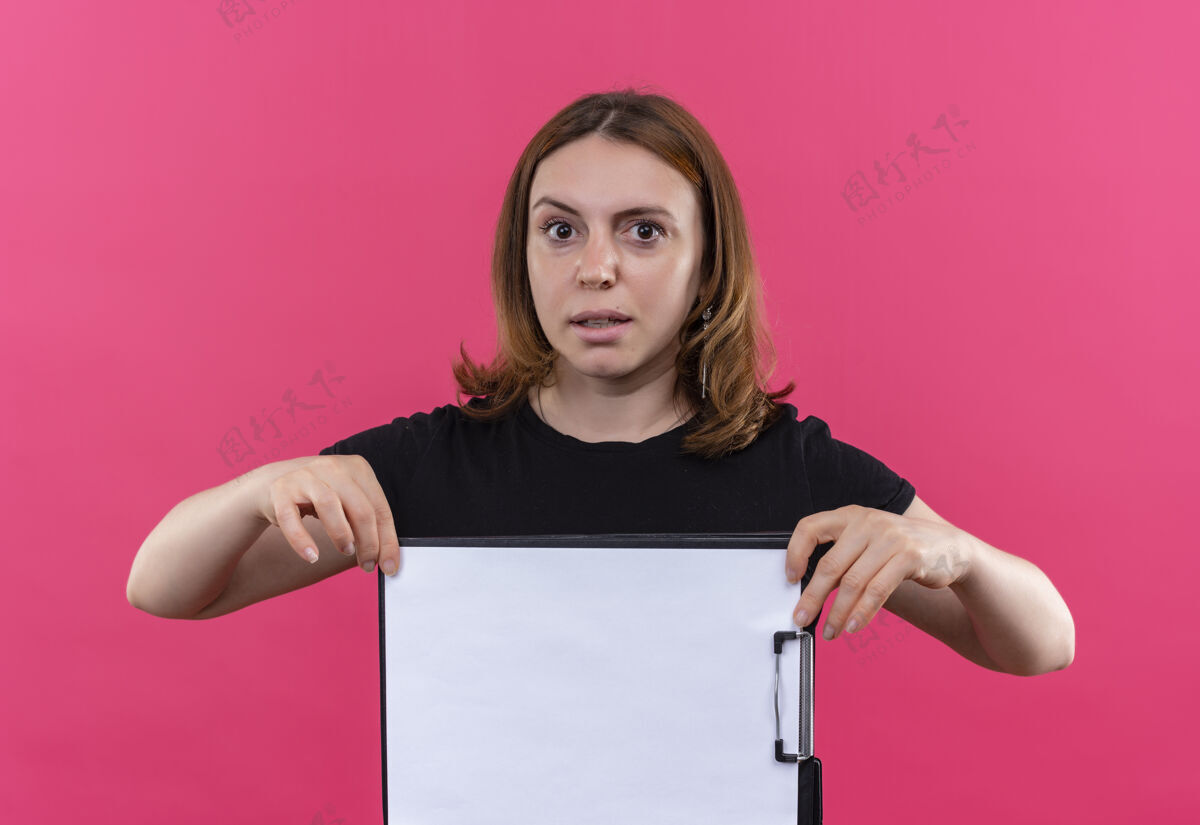 剪贴板年轻随意的女人拿着剪贴板 站在孤立的粉红色墙上女人随便拿着
