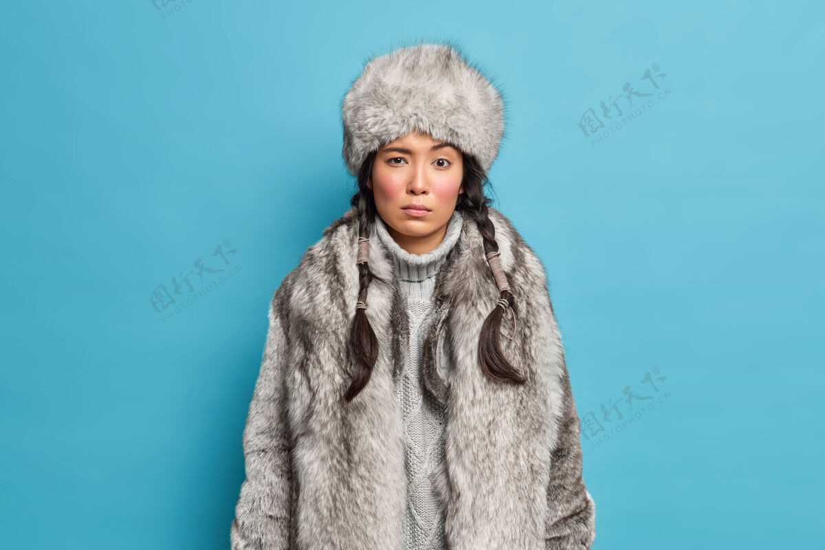 时尚美丽严肃的女人站在前面 穿着冬天的帽子外套 在寒冷的天气里在蓝色的墙上摆姿势穿外套的圣诞女孩女性圣诞节个人