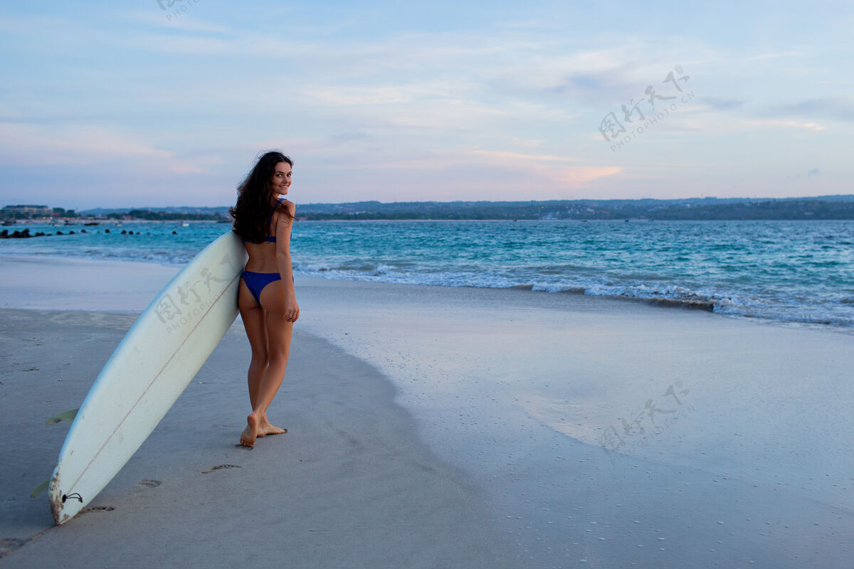 女性美丽的女孩拿着冲浪板站在沙滩上阳光热带运动