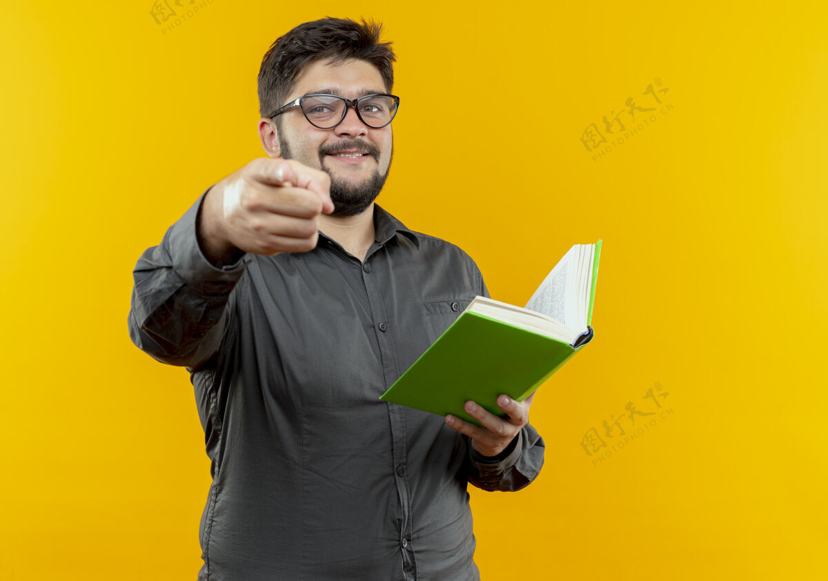 握着面带微笑的年轻商人戴着眼镜拿着书 在黄色的墙上给你们看商人眼镜戴着
