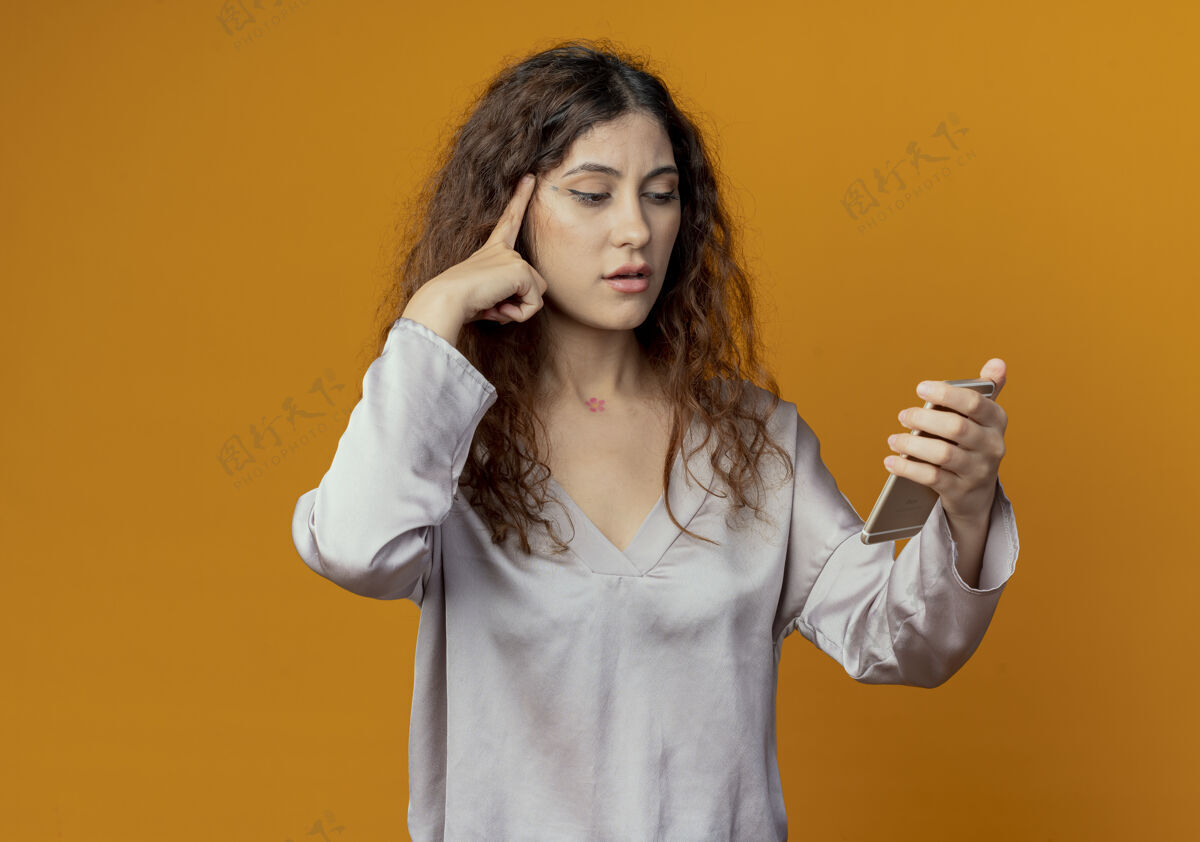 年轻想着年轻漂亮的女孩拿着手机 看着手机 把手指放在隔离在黄色墙上的头上电话女孩头