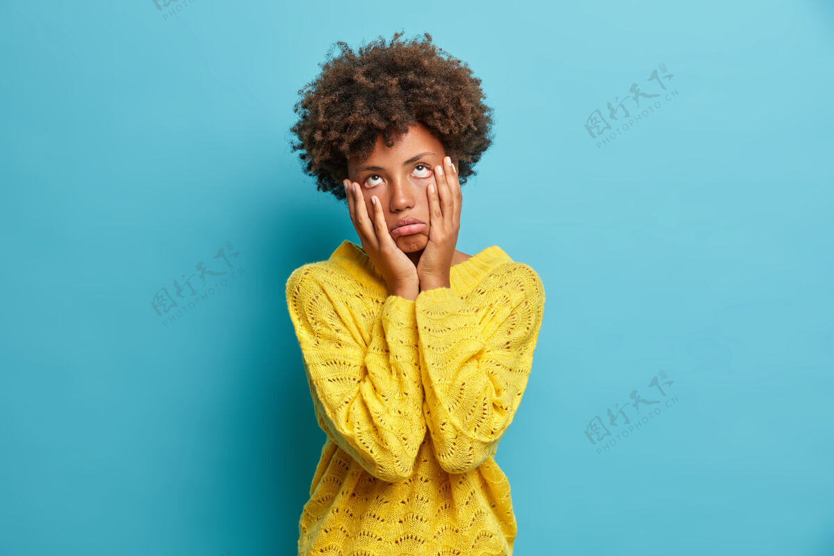 不快乐失望悲伤疲惫的女人摸着脸颊 看起来很无聊 考试失败后感觉很不开心穿着黄色毛衣对着蓝色的墙摆姿势年轻消极随意