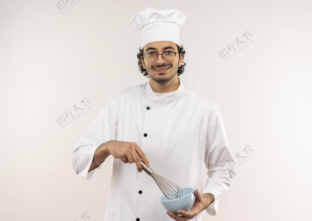 年轻面带微笑的年轻男厨师穿着厨师制服 戴着眼镜 手里拿着威士忌和碗 隔离在白色的墙上拂烹饪制服