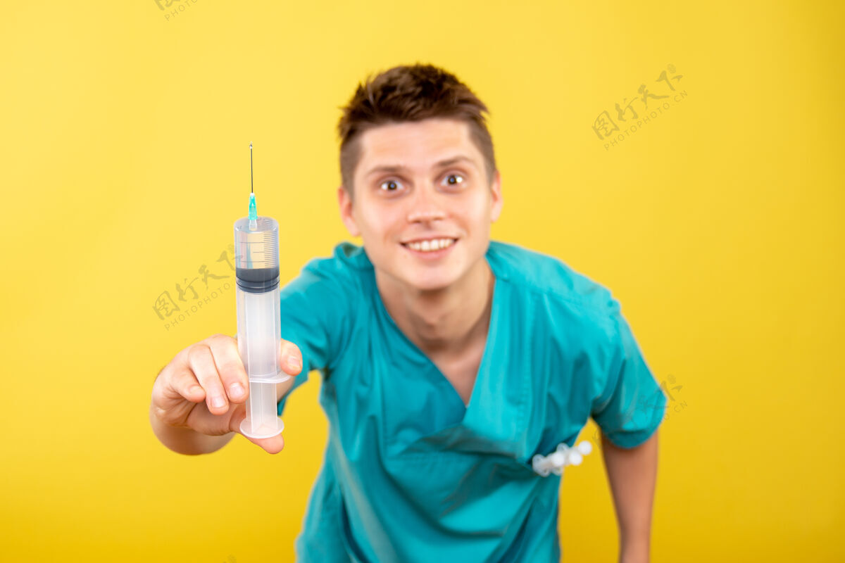药正面图黄色背景上穿着医疗服拿着针剂的年轻男医生西装人年轻的男医生