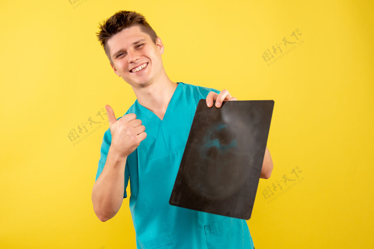 男性正面图黄色背景上穿着医疗服拿着x光片的年轻男医生X光人人