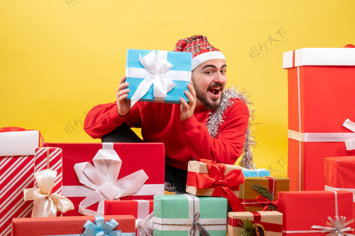 礼物正面图：坐在黄色背景上的年轻男性礼物盒子周围年