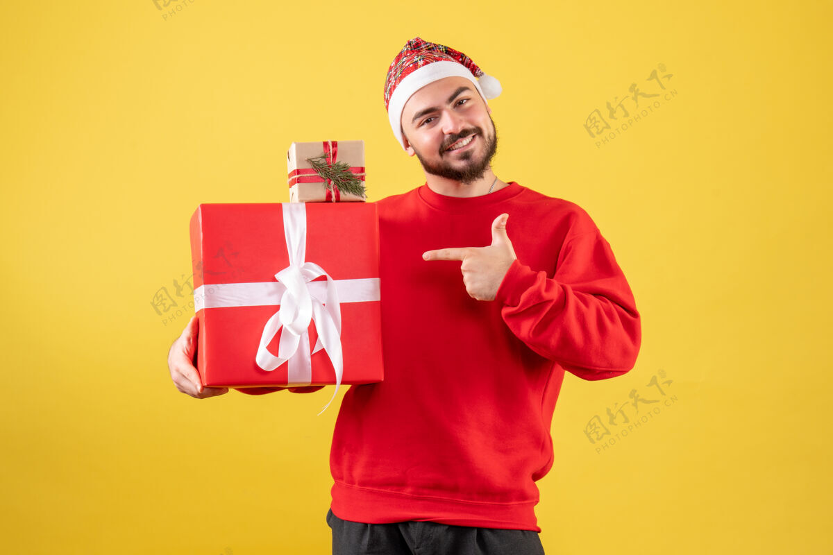 人黄色背景下手持圣诞礼物的年轻男性正面图年轻男性雪成人