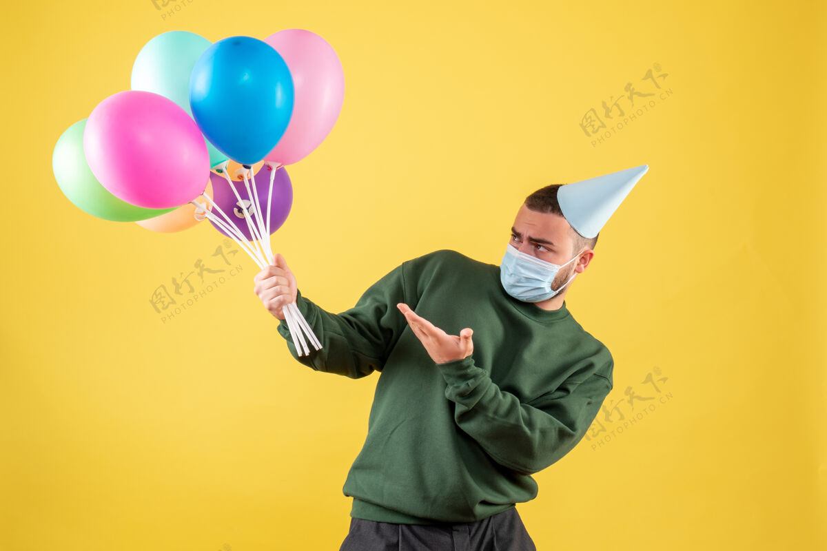 乐趣正面图黄色背景上手持彩色气球的年轻男性流行病庆祝背景