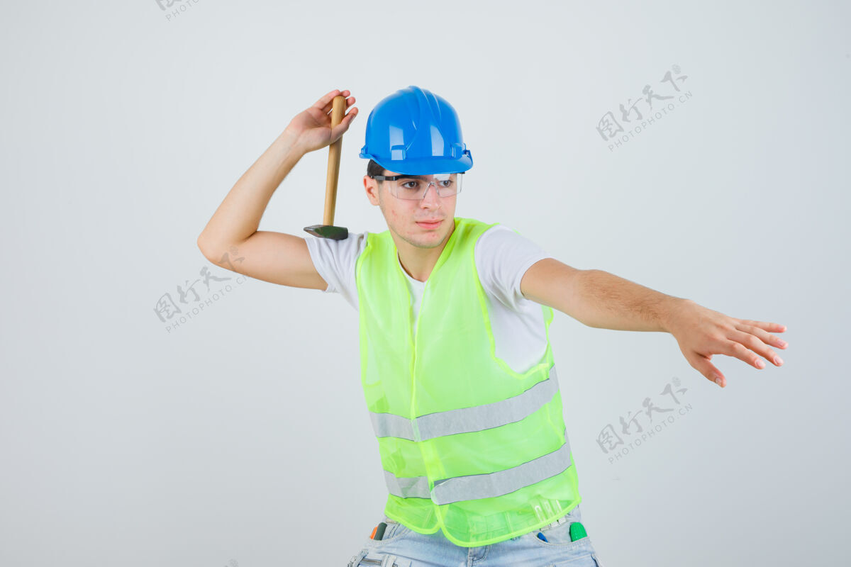 扔年轻的男孩拿着锤子 试图把它扔在建筑制服 并期待着集中精力 前视图年轻微笑教育