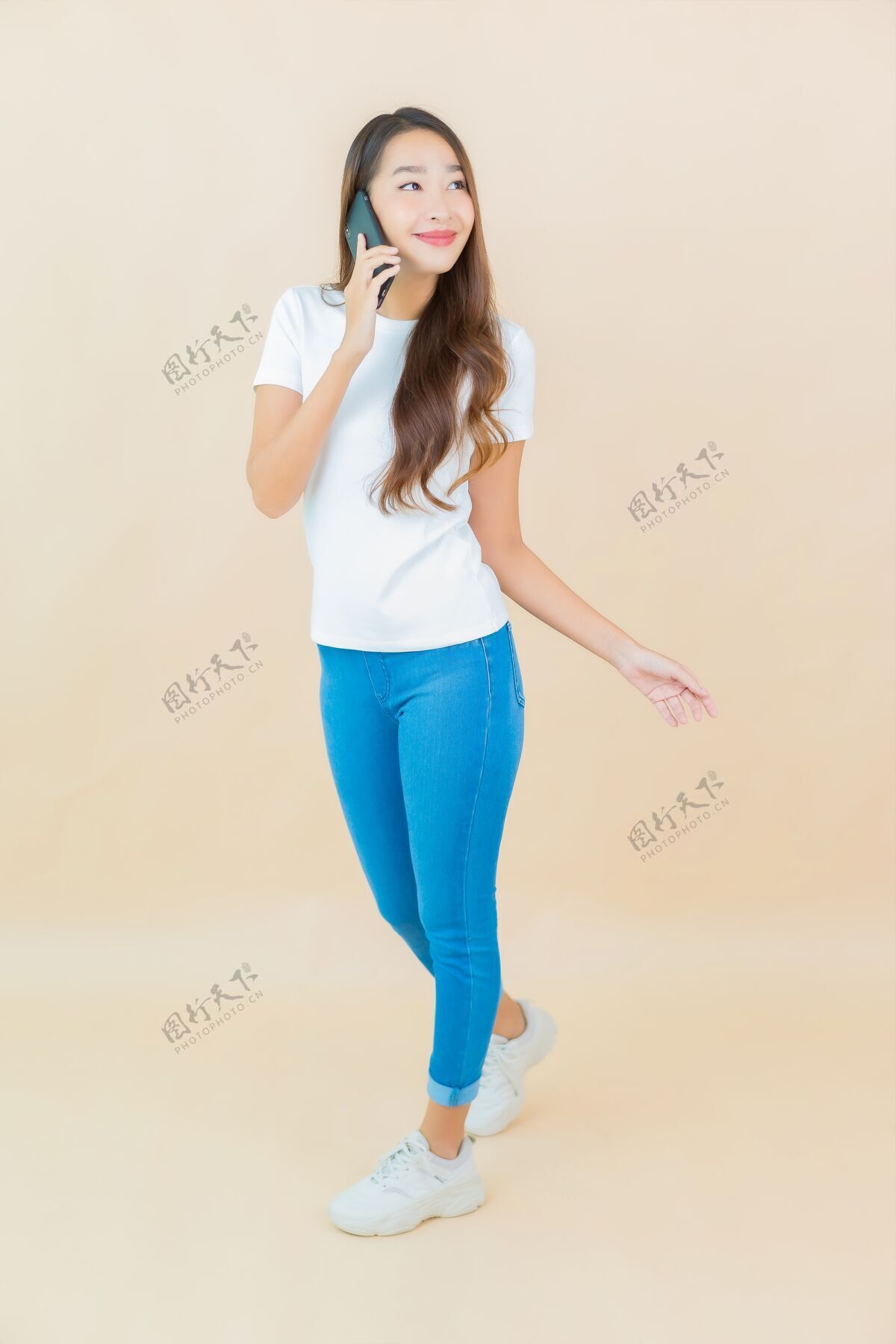 手机肖像美丽的亚洲年轻女子在米色上使用智能手机电话站着快乐