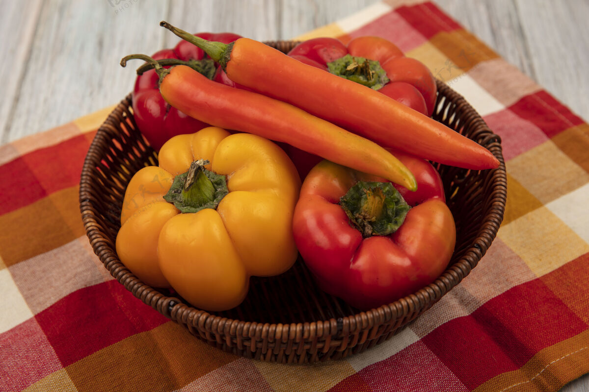 蔬菜灰色木墙上格子布上的桶上五颜六色的新鲜辣椒的俯视图有机桶胡椒