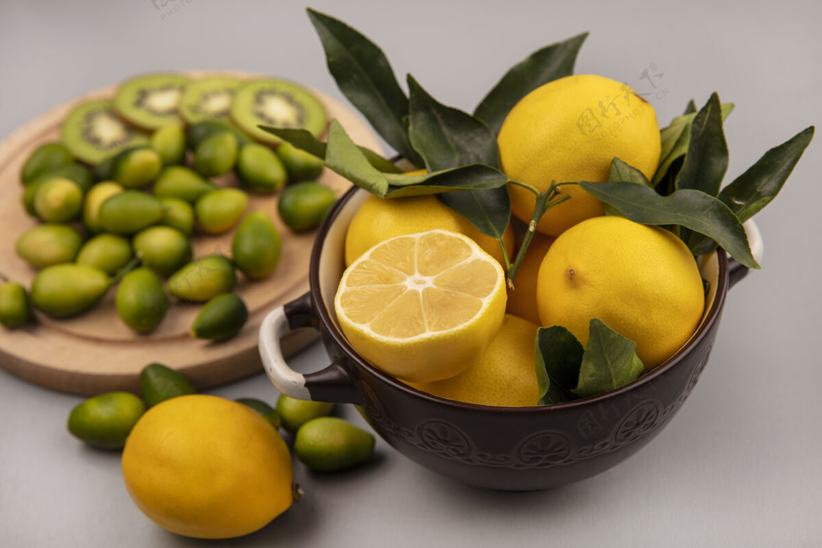 柑橘白色墙壁上的木制厨房板上 碗上放着黄色柠檬 碗里放着金盏花和猕猴桃片碗切片配料