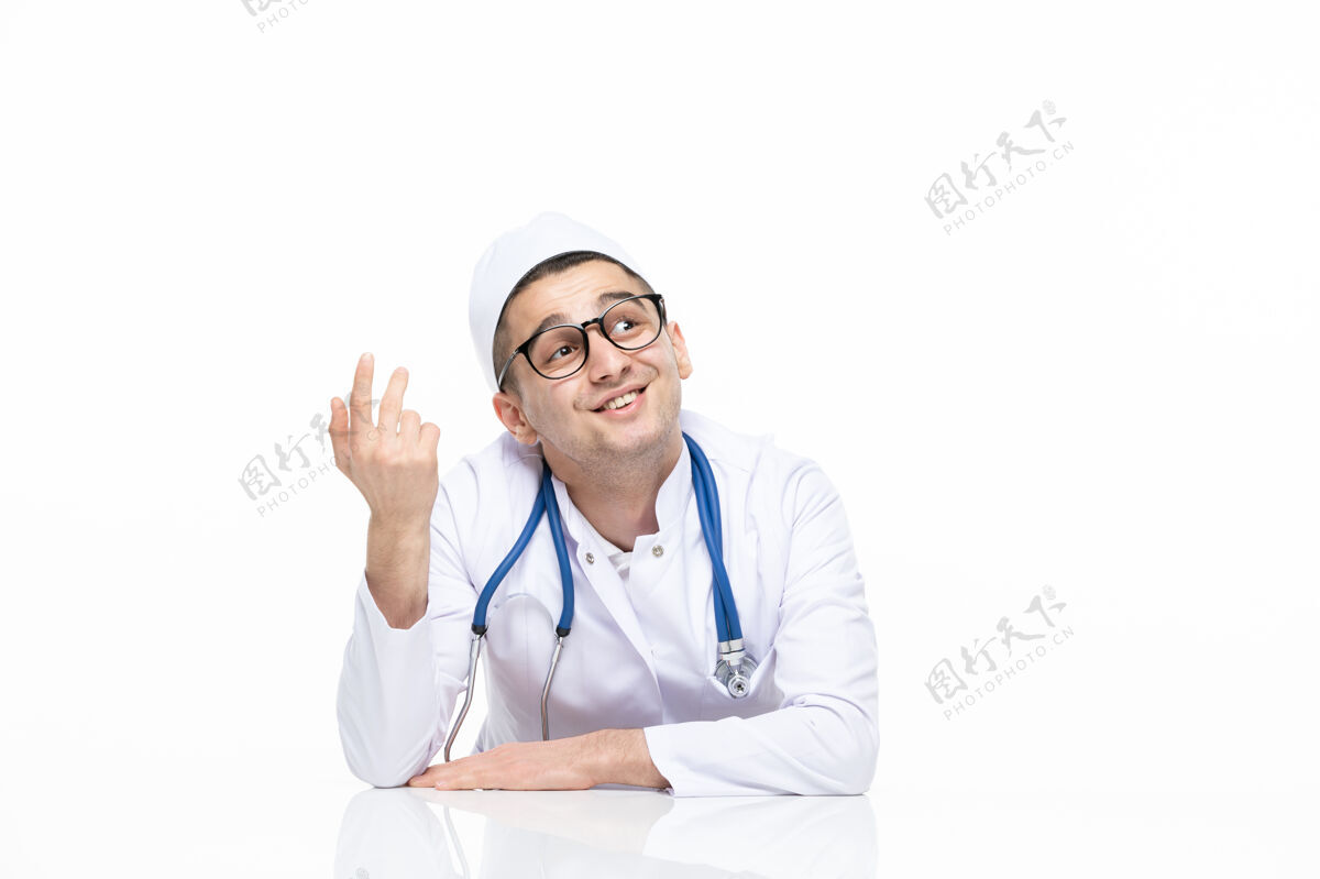 年轻人正面图：年轻的思维医生 穿着医疗服 坐在白墙上的桌子后面护士听诊器微笑