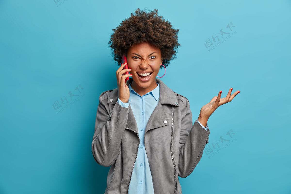 抱着沮丧烦躁的黑皮肤卷发女人举手 有电话交谈 穿着时髦的衣服 手势活跃 人类成人美国