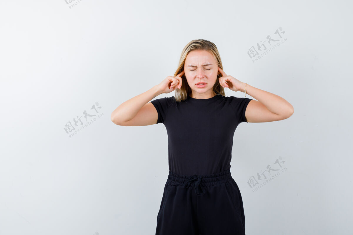 乐趣年轻女士用手指塞住耳朵 穿着t恤 裤子 看上去很苦恼正视图肖像女人头发