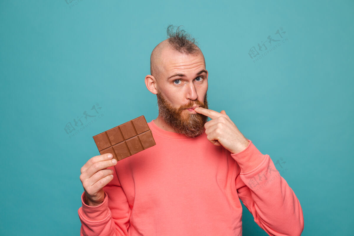 糖果留着胡须的欧洲男人在随意的桃子里孤立 手捧美味的巧克力舔手指年轻食物酒吧