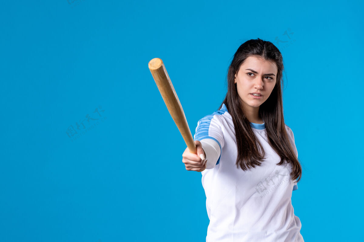 成人正面图蓝色墙上拿着棒球棒的年轻女子前面体育棒球