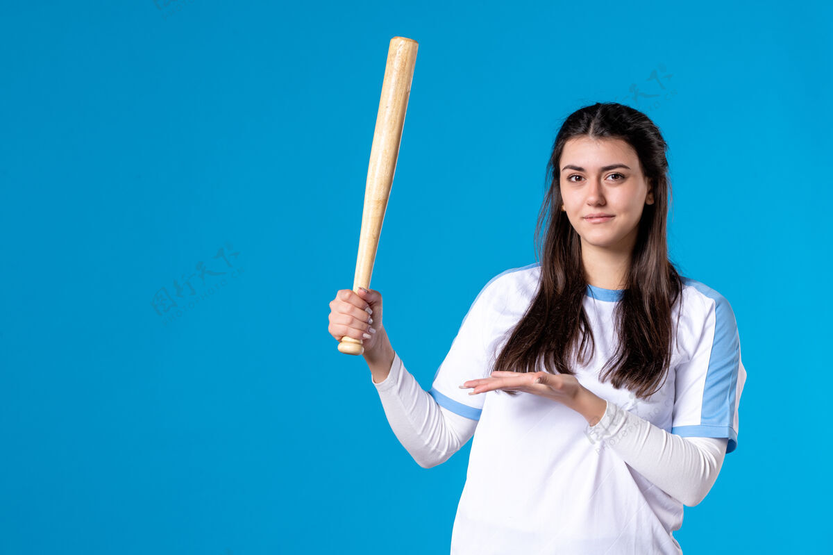 视图正面图蓝色墙上拿着棒球棒的年轻女子成人展示比赛