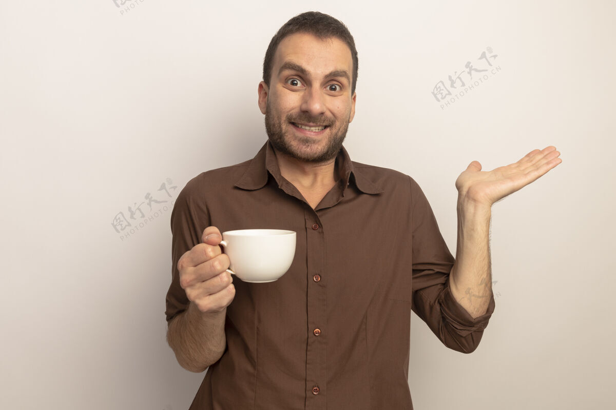 笑微笑着的年轻白人男子端着一杯茶 看着镜头 在白色的背景上 一只空手孤立着 留着复印空间杯抱复制