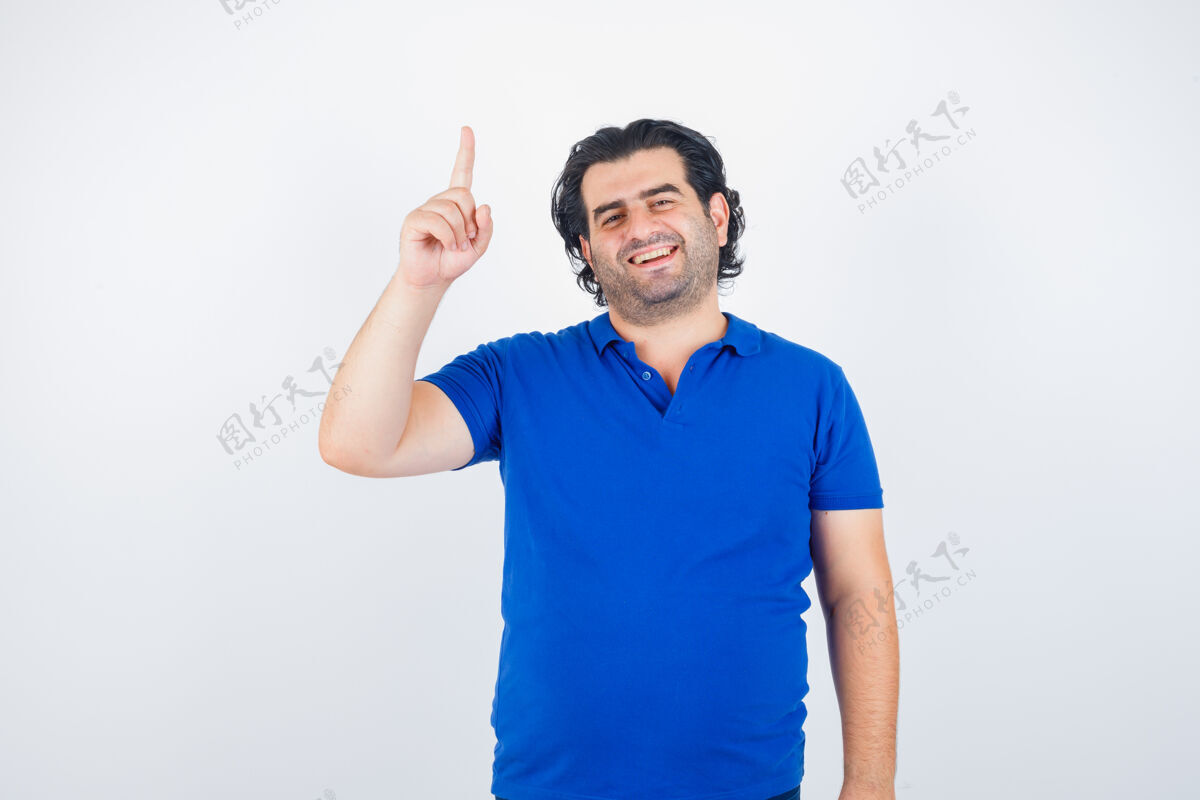 年轻成熟男人举起食指在尤里卡手势在蓝色t恤 牛仔裤和看起来理智 前视图男性复古牛仔裤