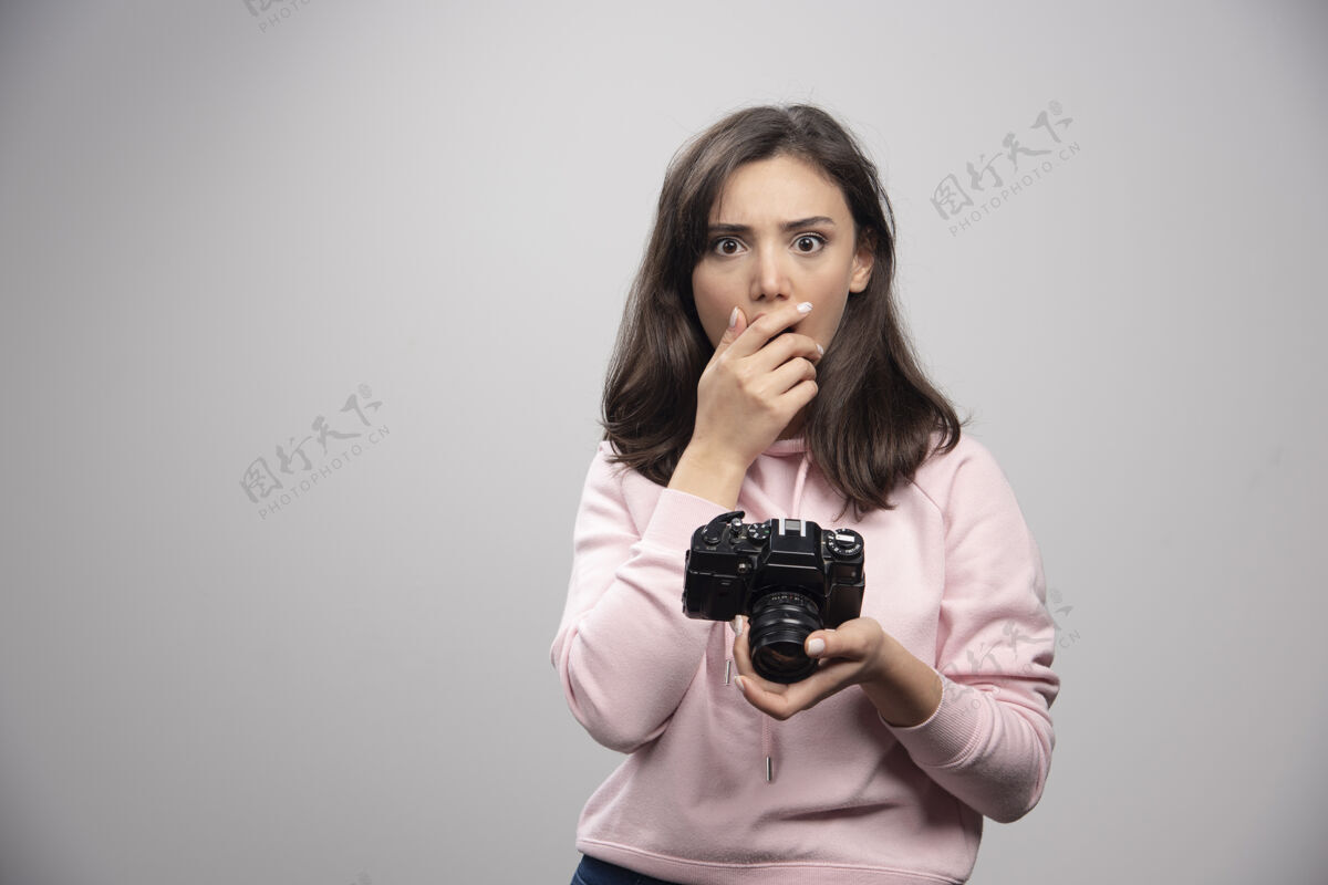 女孩美丽的年轻女子站在灰色的墙上 拿着相机人漂亮女人
