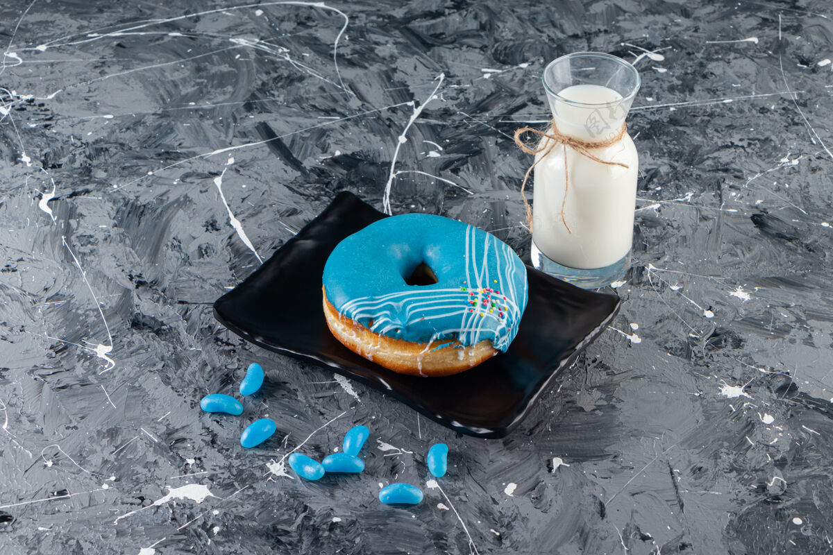 烘焙蓝色甜甜圈加奶油糖霜和一杯牛奶放在大理石桌上釉面包房曲奇