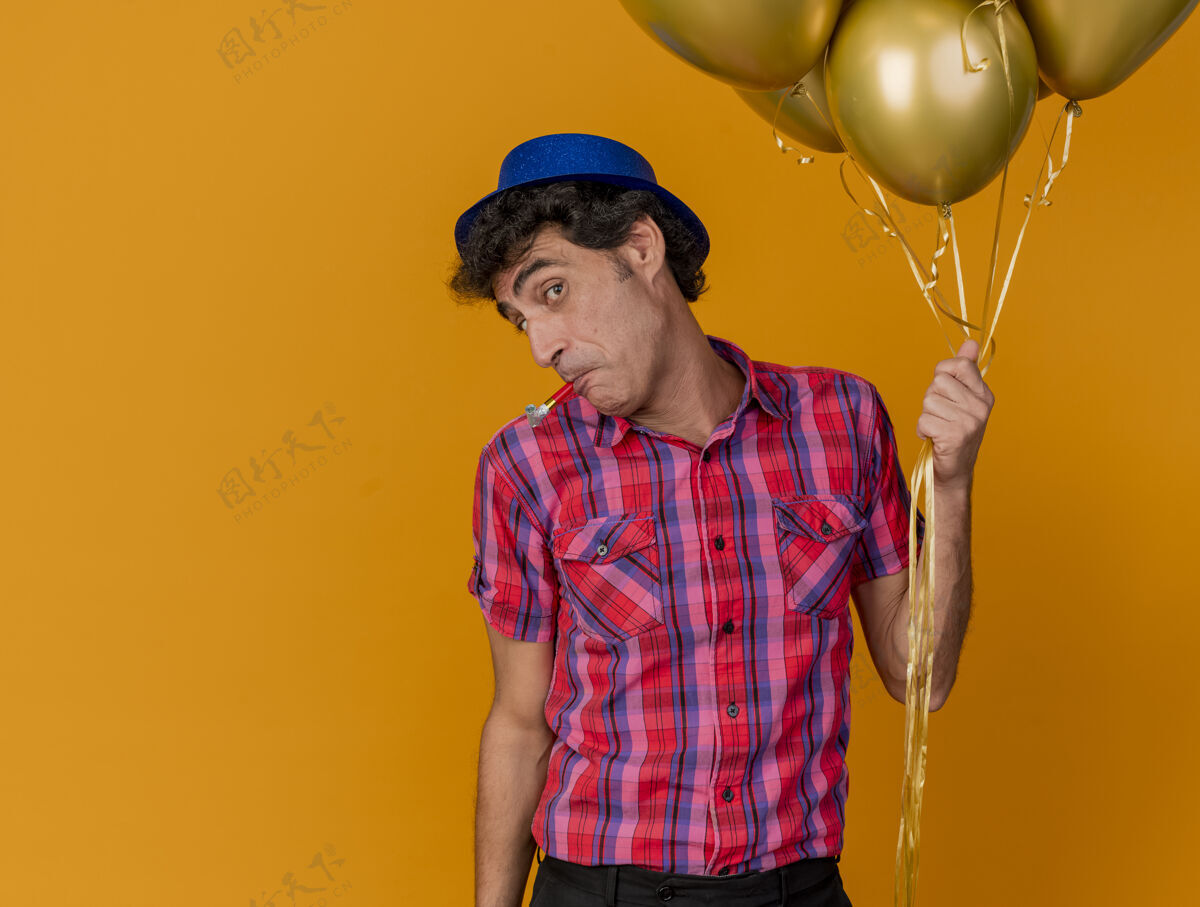 嘴令人印象深刻的中年党人戴着党的帽子拿着气球看着前面的党吹嘴孤立在橙色的墙上人气球穿着
