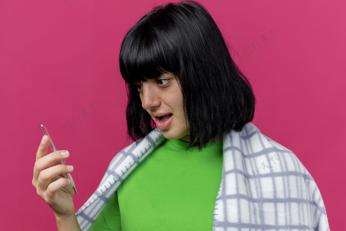 姿势特写镜头中 年轻的生病妇女裹着格子布 手持隔离在粉红色墙上的温度计人脸疾病