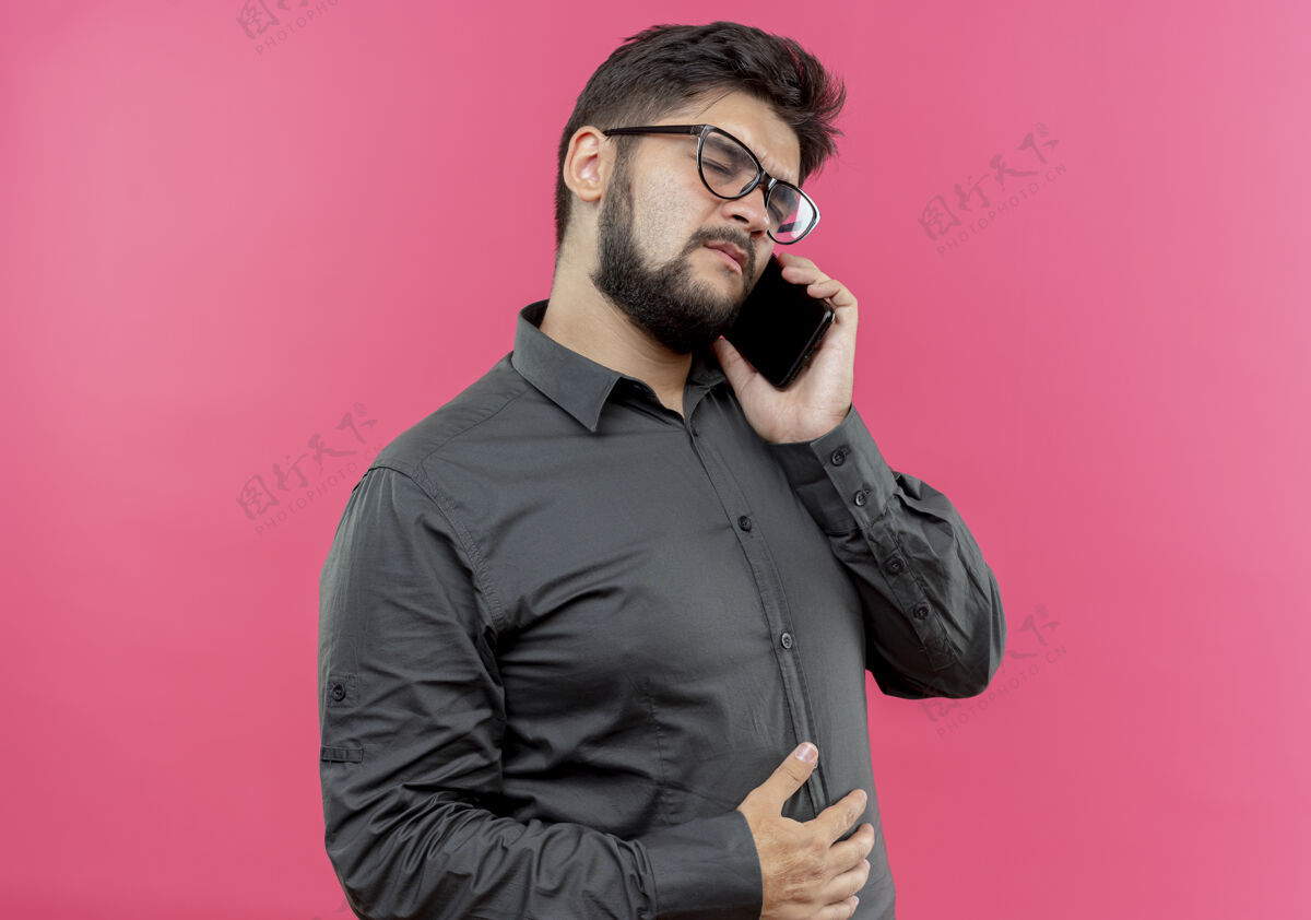 年轻戴着眼镜的年轻商人闭着眼睛在电话里说话 粉红色的脸上孤立着闭嘴眼镜手势