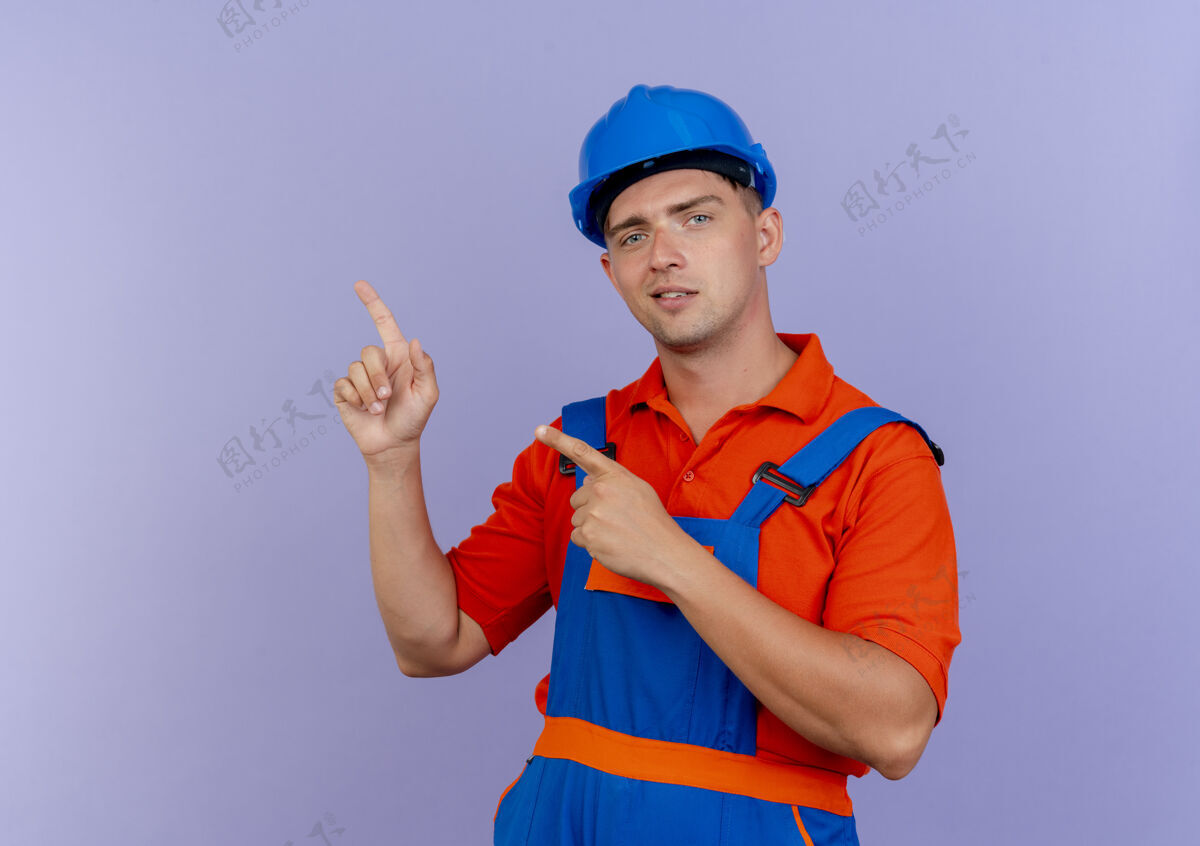 年轻高兴的年轻男子建设者身穿制服和安全帽点在紫色边上建设者男性安全