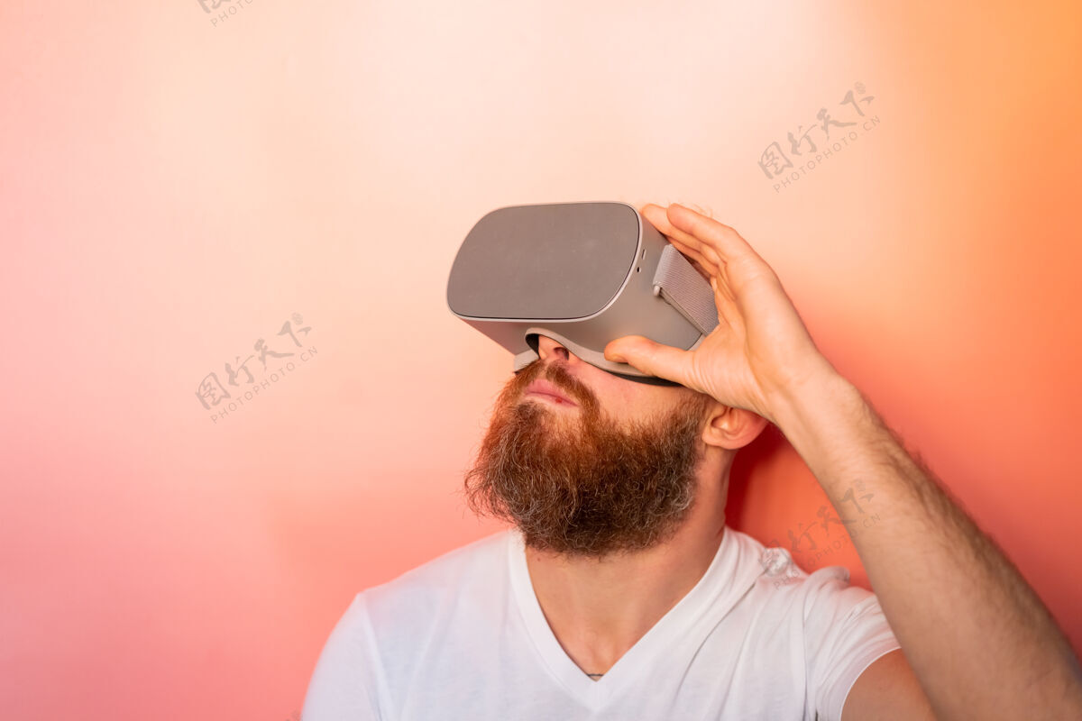 胡须一个留着胡子的男人在工作室里戴着虚拟现实眼镜 背景是粉橙色的 这是一幅感人的肖像乐趣眼镜创意