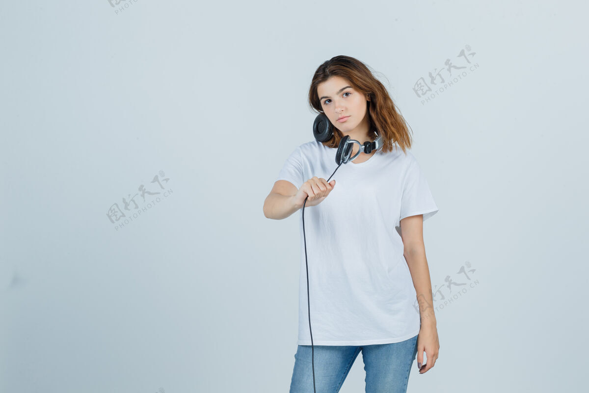 成人年轻的女性手持耳机 穿着白色t恤 牛仔裤 看上去很诱人 前视图肖像人微笑