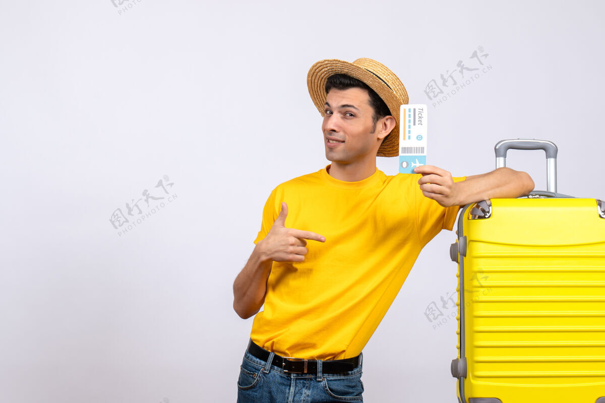 微笑正面图酷酷的年轻游客站在黄色手提箱旁指着车票乐趣帽子快乐