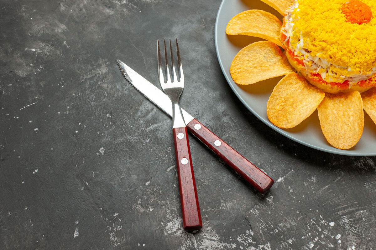 晚餐沙拉的顶视图在右上方 刀叉交叉在黑色背景上沙拉厨具刀