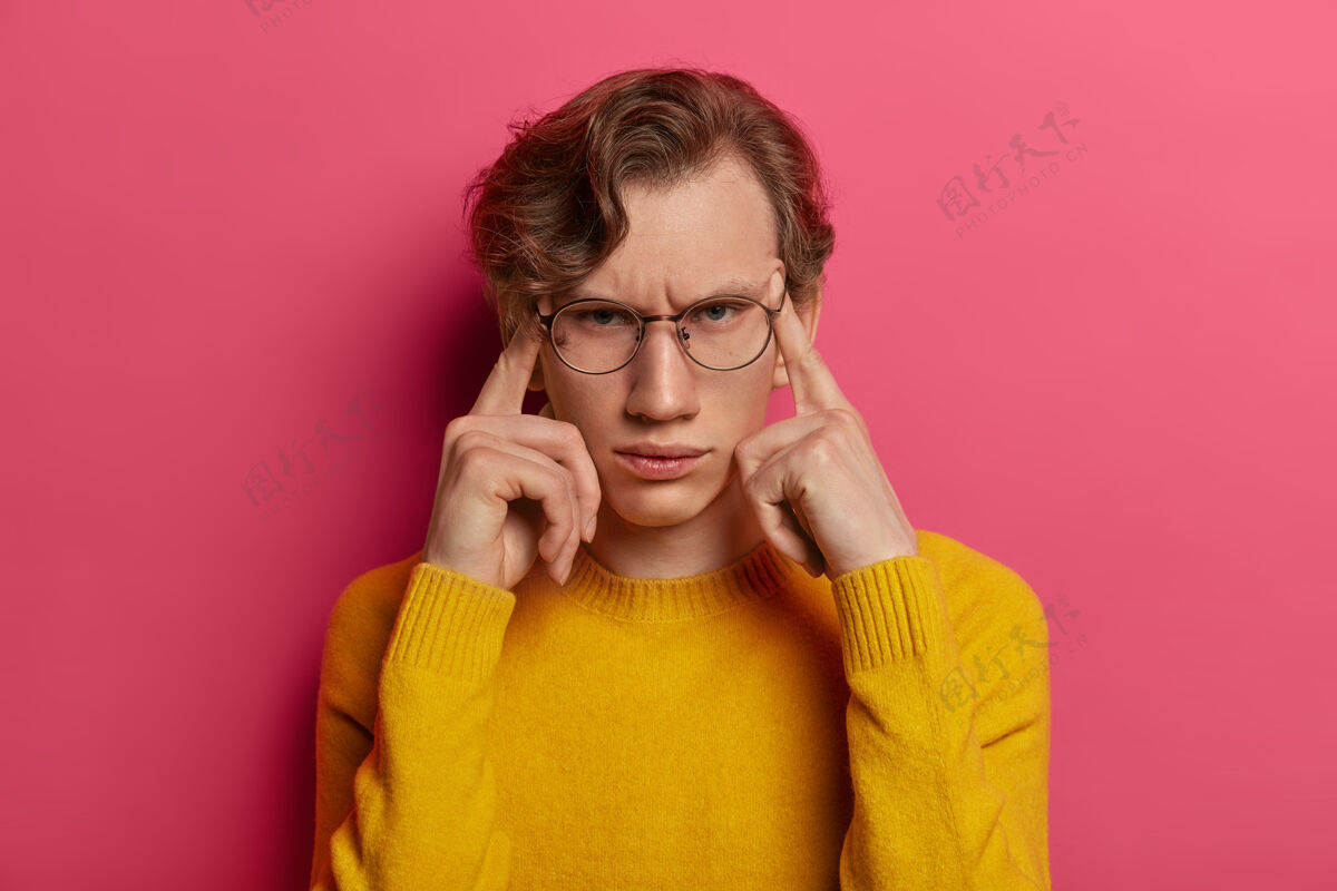 疲惫不满意男人的照片头痛 皱眉 用手指触摸太阳穴 试图集中注意力 记得什么 戴眼镜 黄色毛衣 孤立在粉红色的墙上痛苦压力男性