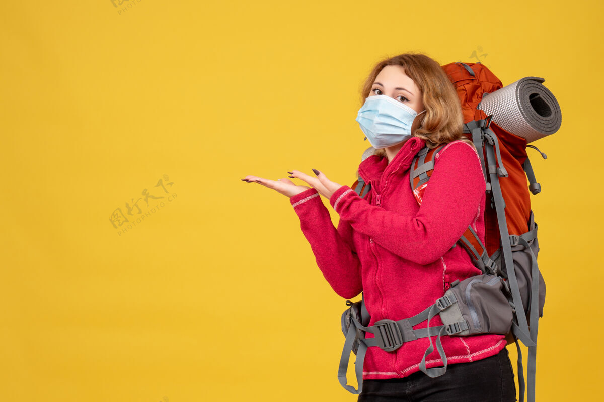 成人俯视图：戴着医用面罩的年轻旅行女孩正在收拾行李 并指向右边的东西指漂亮肖像