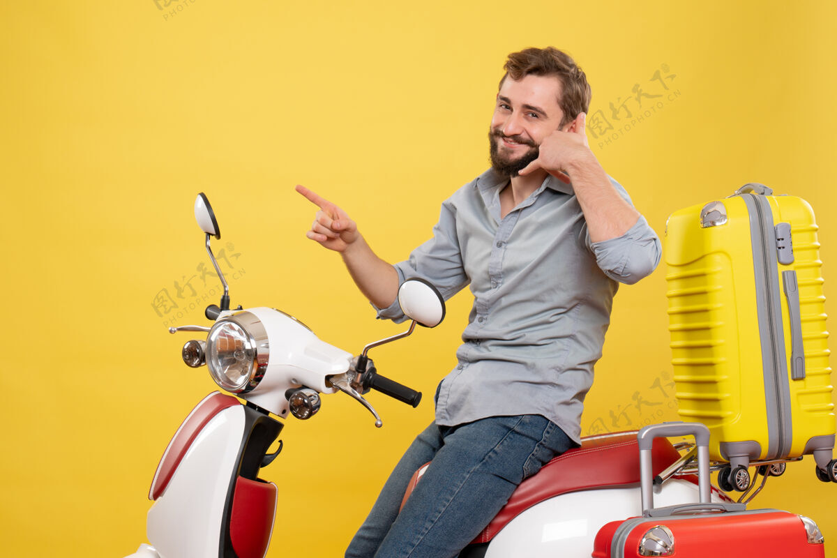 自行车旅游概念的正面视图 微笑的年轻人坐在摩托车上 背着手提箱 在黄色上做着“打电话给我”的手势手势品牌车辆