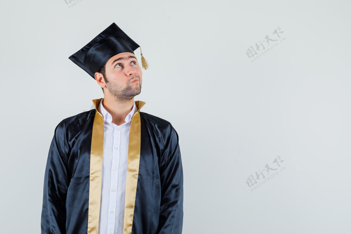 男人年轻人穿着毕业制服向上看 神情犹豫不决 前视图眼镜男人肖像