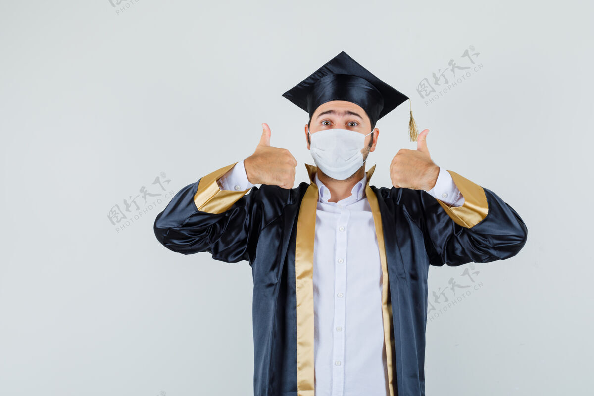 成人穿着毕业制服的年轻人竖起大拇指 看上去很快乐正视图站立衬衫胡须