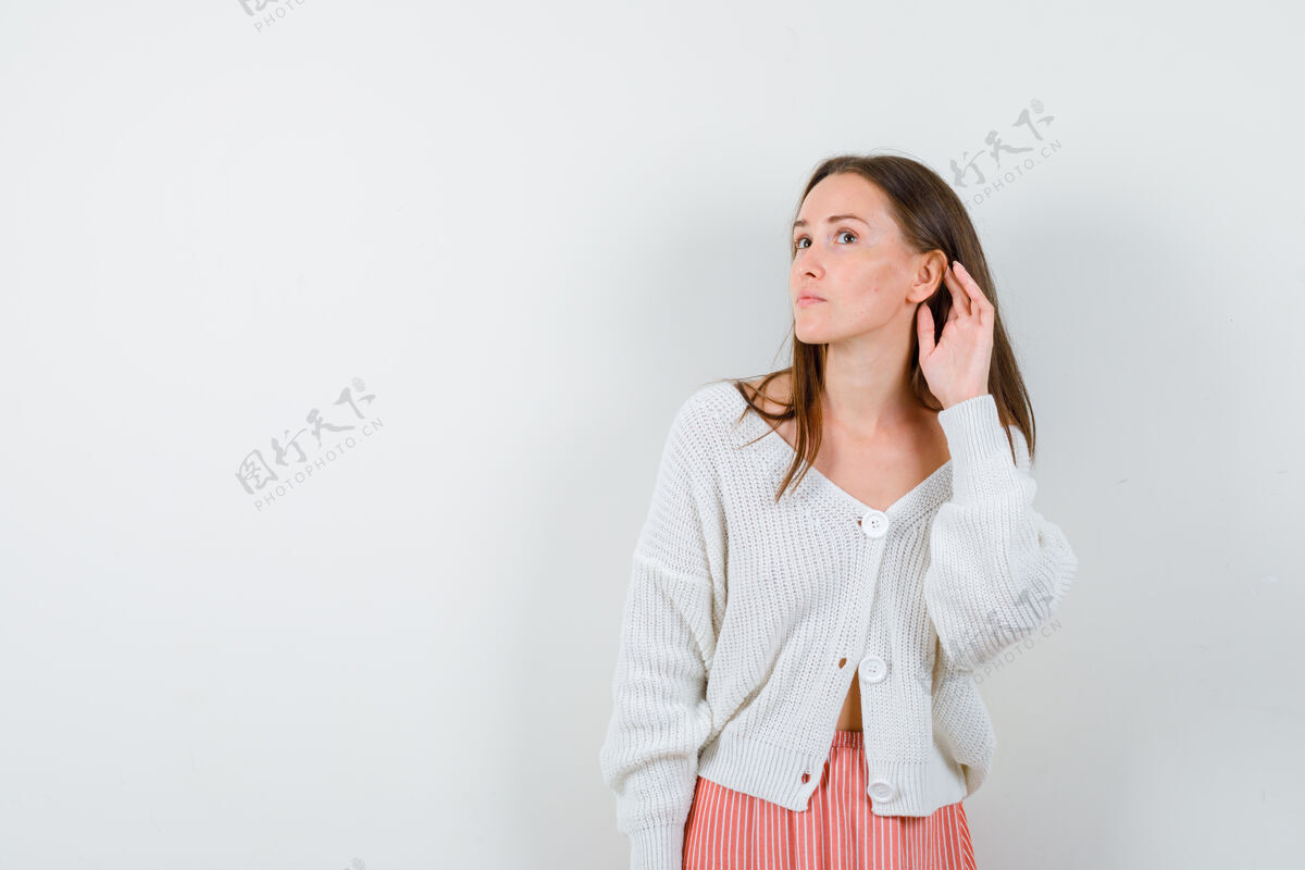 女士穿着开衫和裙子的年轻女性把手放在耳朵后面 看起来很奇怪人欢呼表情