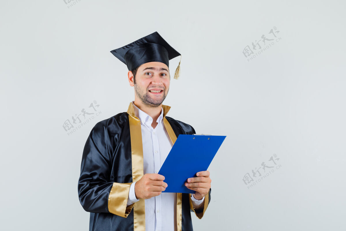欢呼年轻人拿着毕业制服的剪贴簿 看上去兴高采烈 前视模特制服肖像