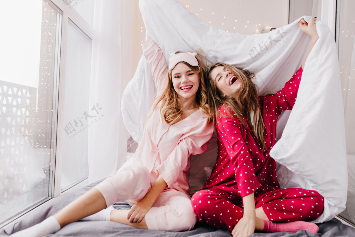 醒来可爱的年轻女子穿着粉红色的睡衣和袜子微笑着室内照片热情的笑女孩开玩笑 而在卧室摆姿势周末睡衣睡眠