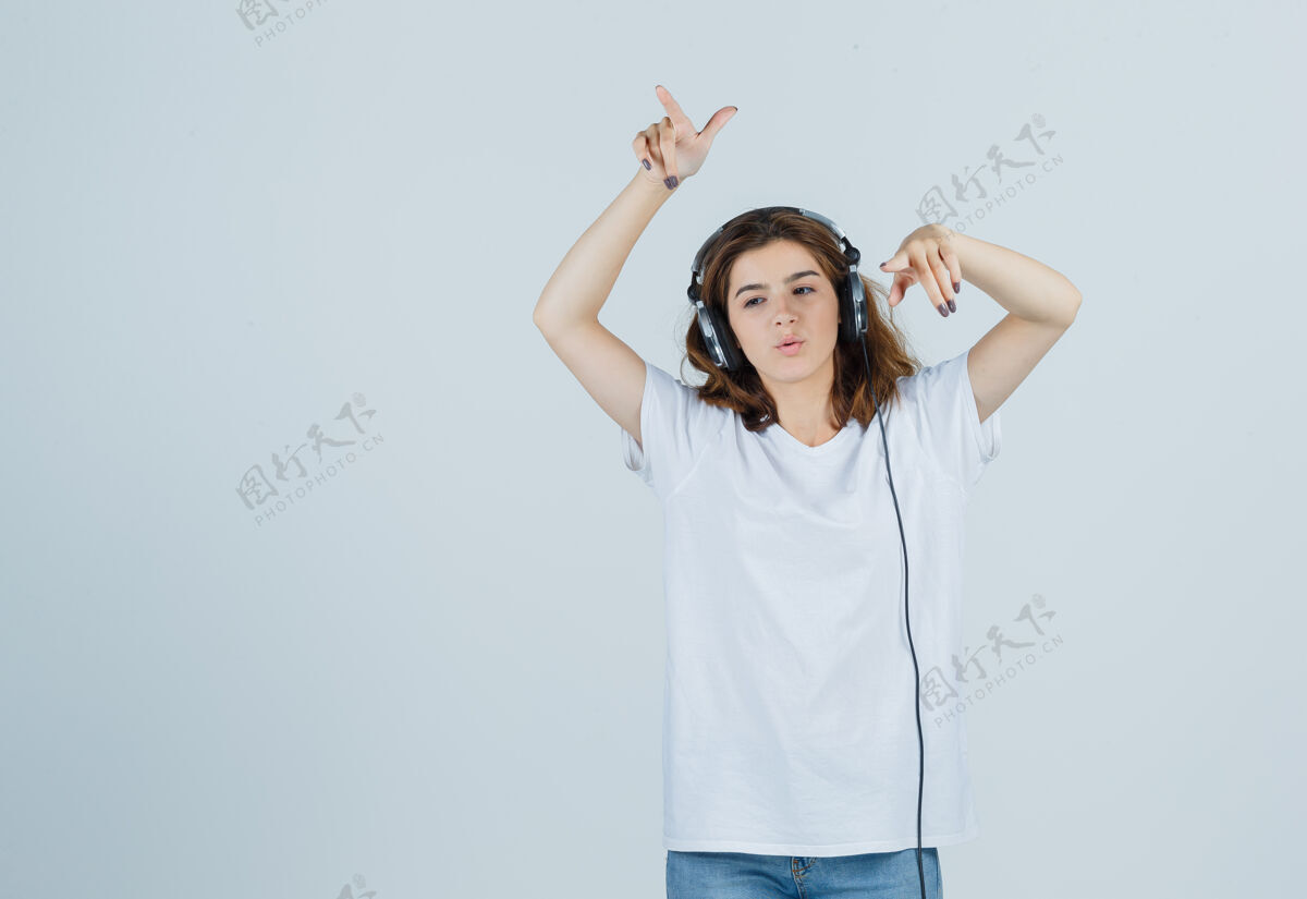 耳机一幅年轻女性的画像 她穿着白色t恤 牛仔裤 戴着耳机一边欣赏音乐 一边看着梦幻般的前景色模特快乐女人