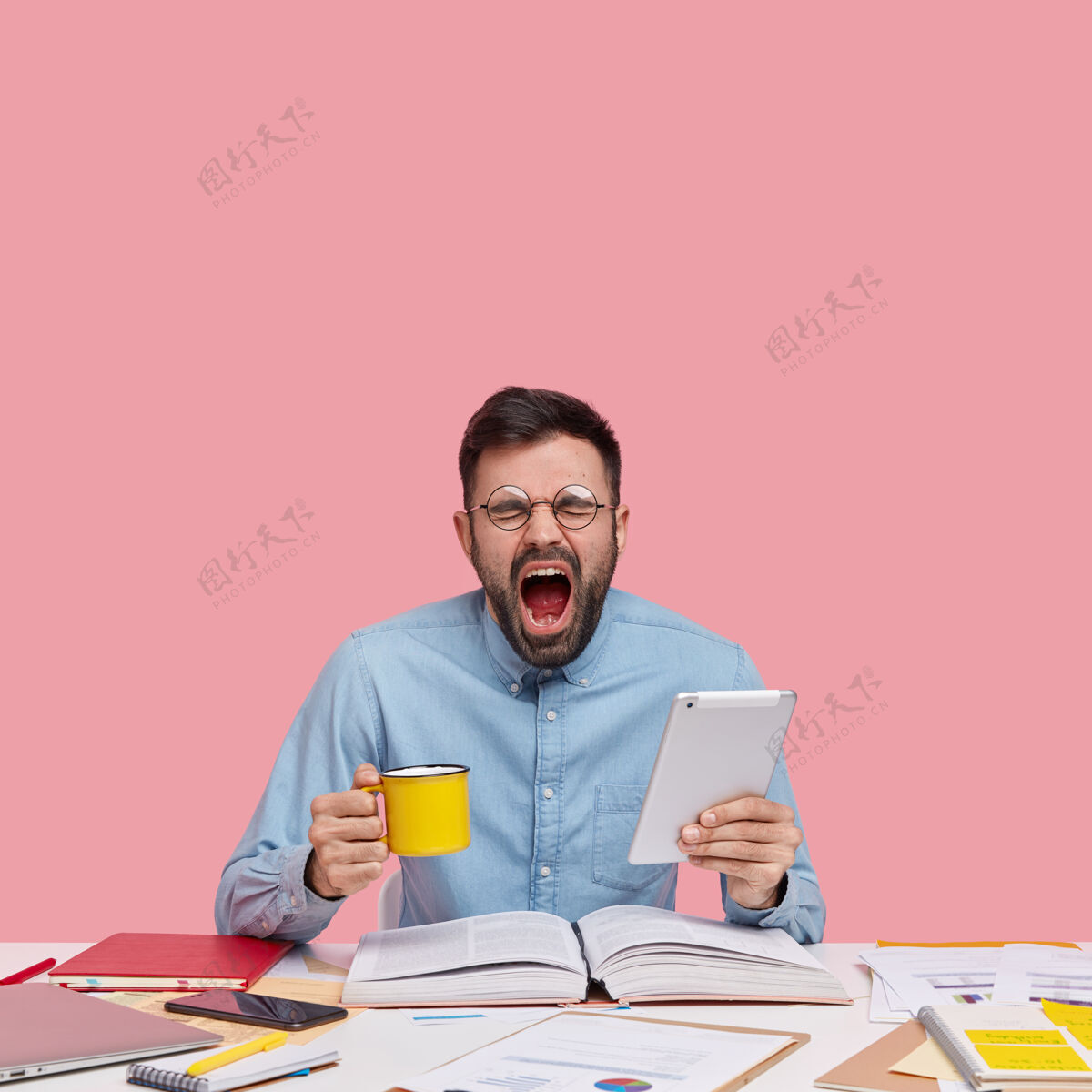 纸学生坐在书桌旁拿着文件拿着杯子和平板电脑累了肖像年轻人