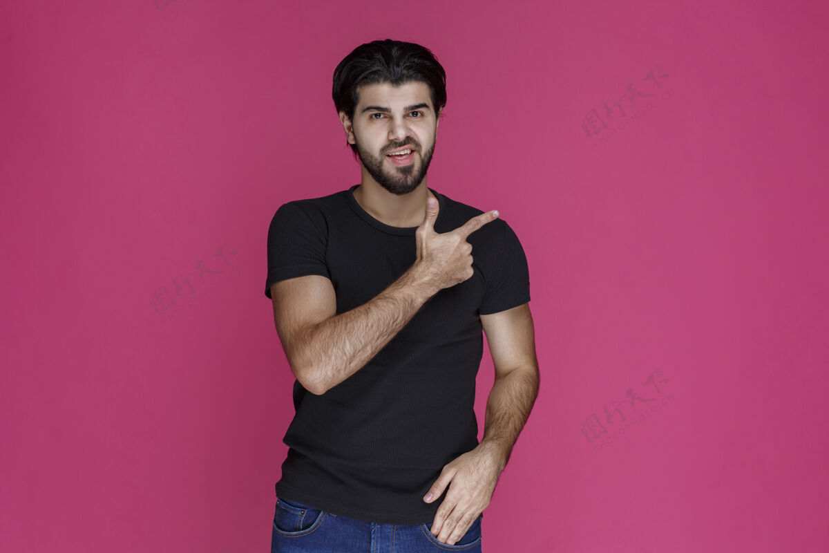 年轻人一个穿着黑衬衫 留着胡子的男人 用一种困惑的方式指着什么东西 或者指明方向方式摆姿势聪明