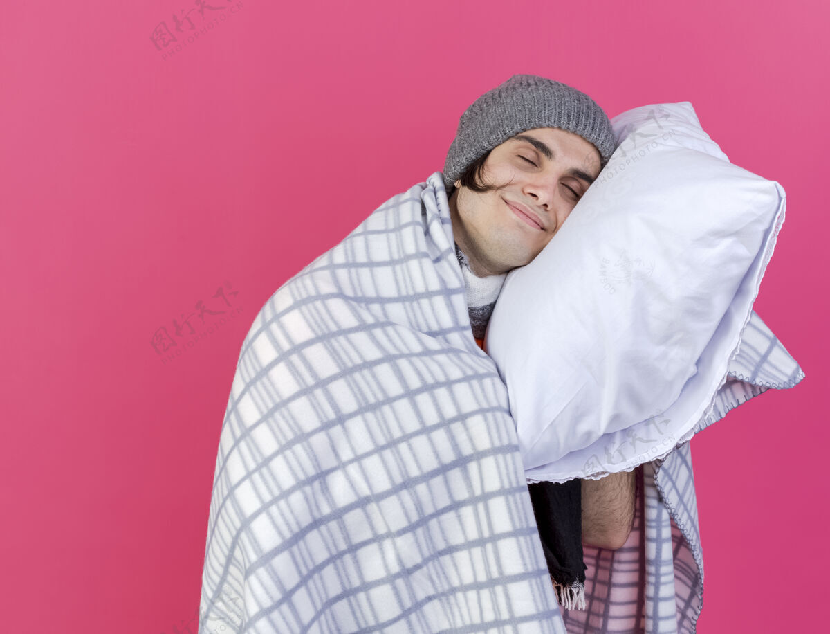 围巾一个戴着冬天帽子 披着格子围巾 头枕在枕头上 背景是粉红色的年轻病患高兴地闭上眼睛疾病头眼睛