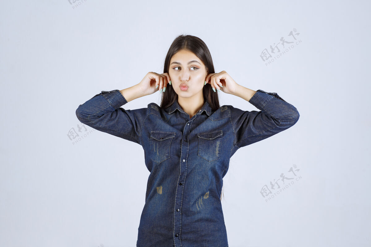噪音一个穿着牛仔衬衫的年轻女人捂着耳朵工人模特女人