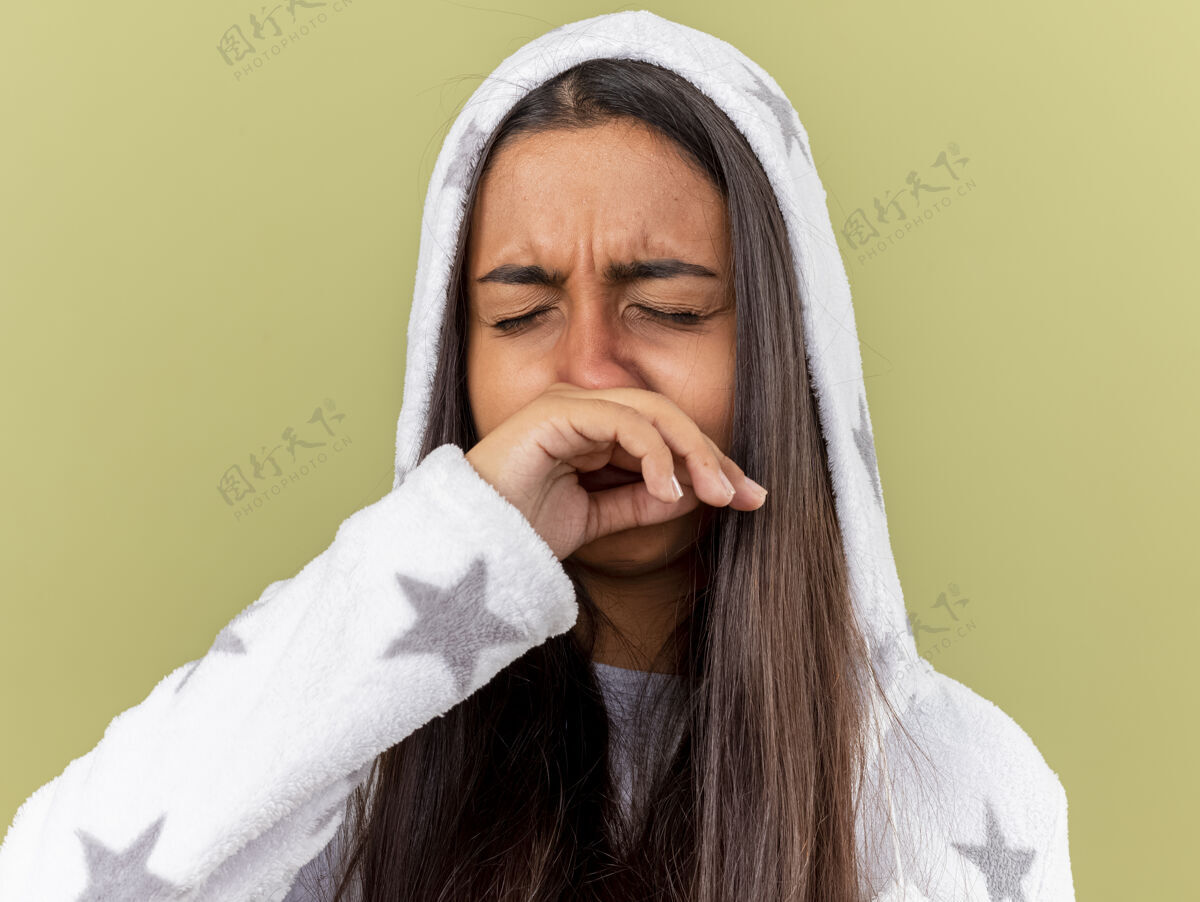 女孩年轻的病女孩闭着眼睛戴上帽子擦鼻子用手隔离在橄榄绿的背景上湿巾眼睛年轻
